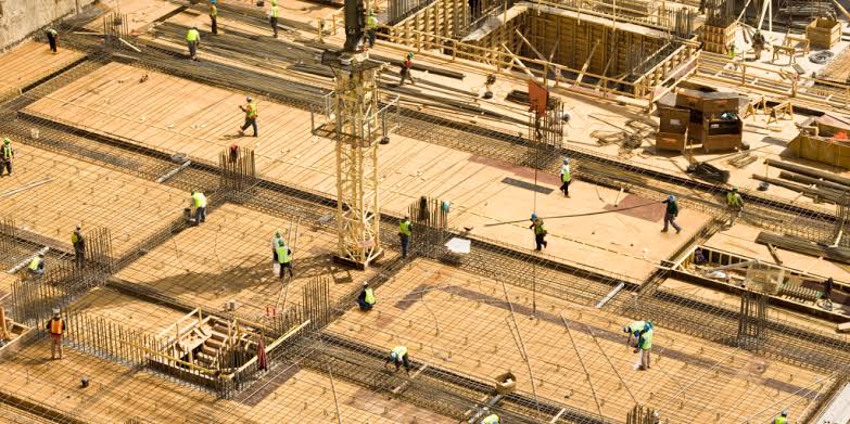 High-angle view of a commercial construction site with workers laying steel rebar grids and foundation formwork, showcasing active commercial property development and real estate investment.