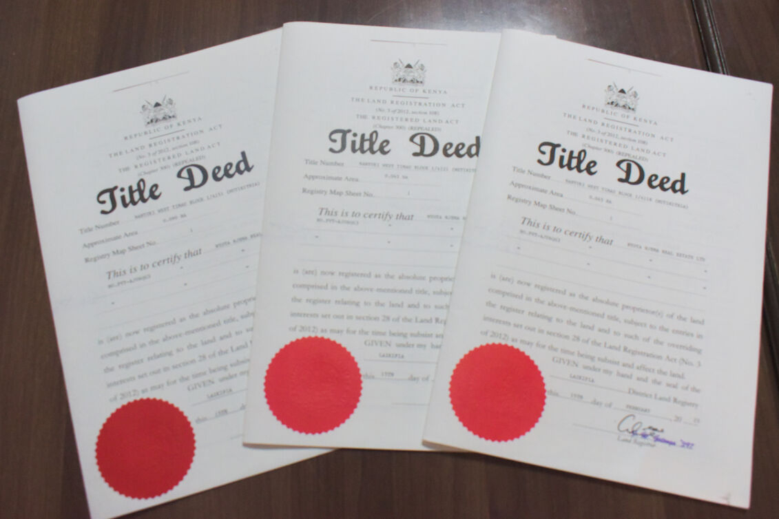 Three official Republic of Kenya legal Title Deed documents spread out on a wooden table, each featuring the coat of arms at the top and a prominent red seal at the bottom.