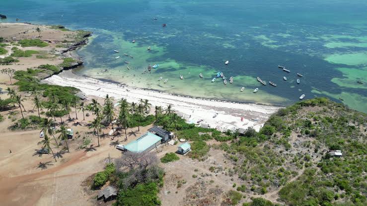 Aerial view of undeveloped beachfront land for sale near Mayungu Beach, Malindi, showing pristine turquoise waters, local fishing boats, and a secure beachfront plot with coconut palms.