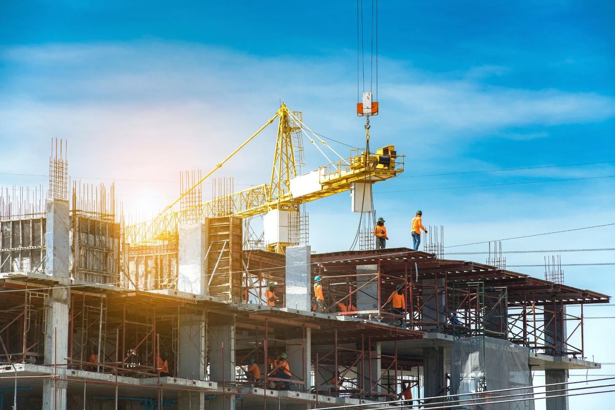 Low-angle view of a multi-storey commercial building under construction with a large yellow tower crane lifting materials, showcasing active property development and real estate investment.