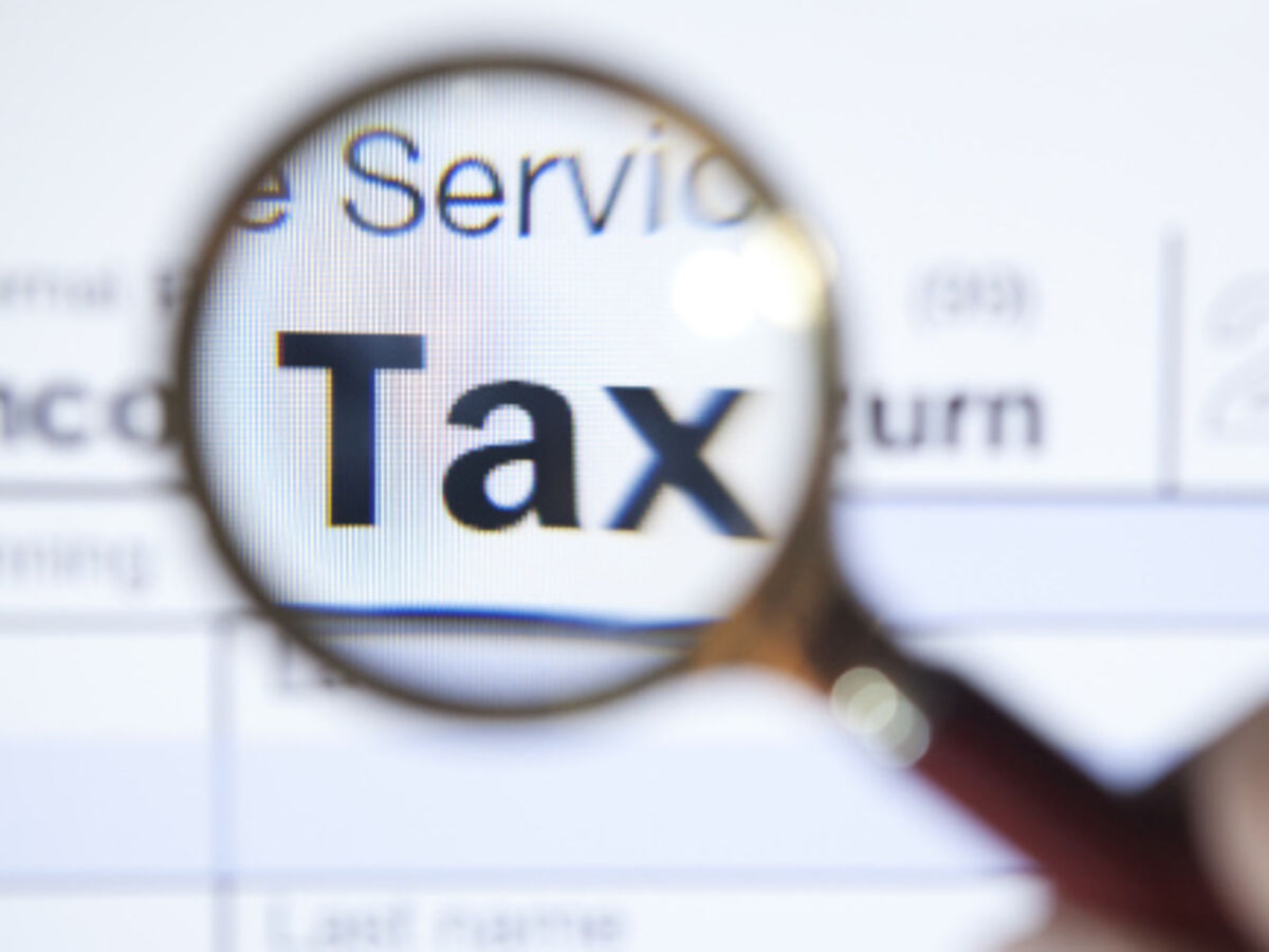 Close-up of a magnifying glass focusing on the word Tax on a financial document, symbolizing real estate tax compliance, property tax deductions, and strategic investment planning.