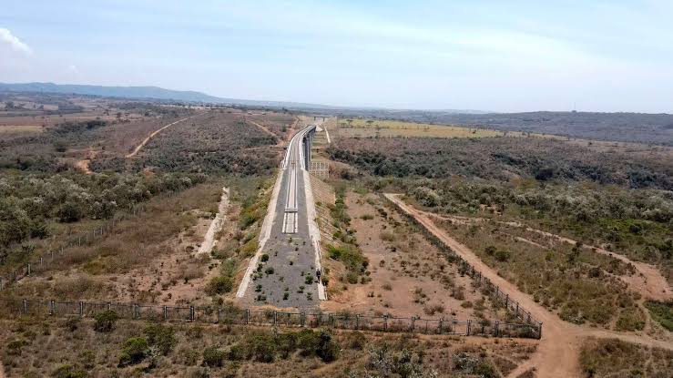 Aerial view of a modern elevated railway bridge and transport corridor cutting through rural land, highlighting infrastructure development that drives nearby property value and land acquisition.